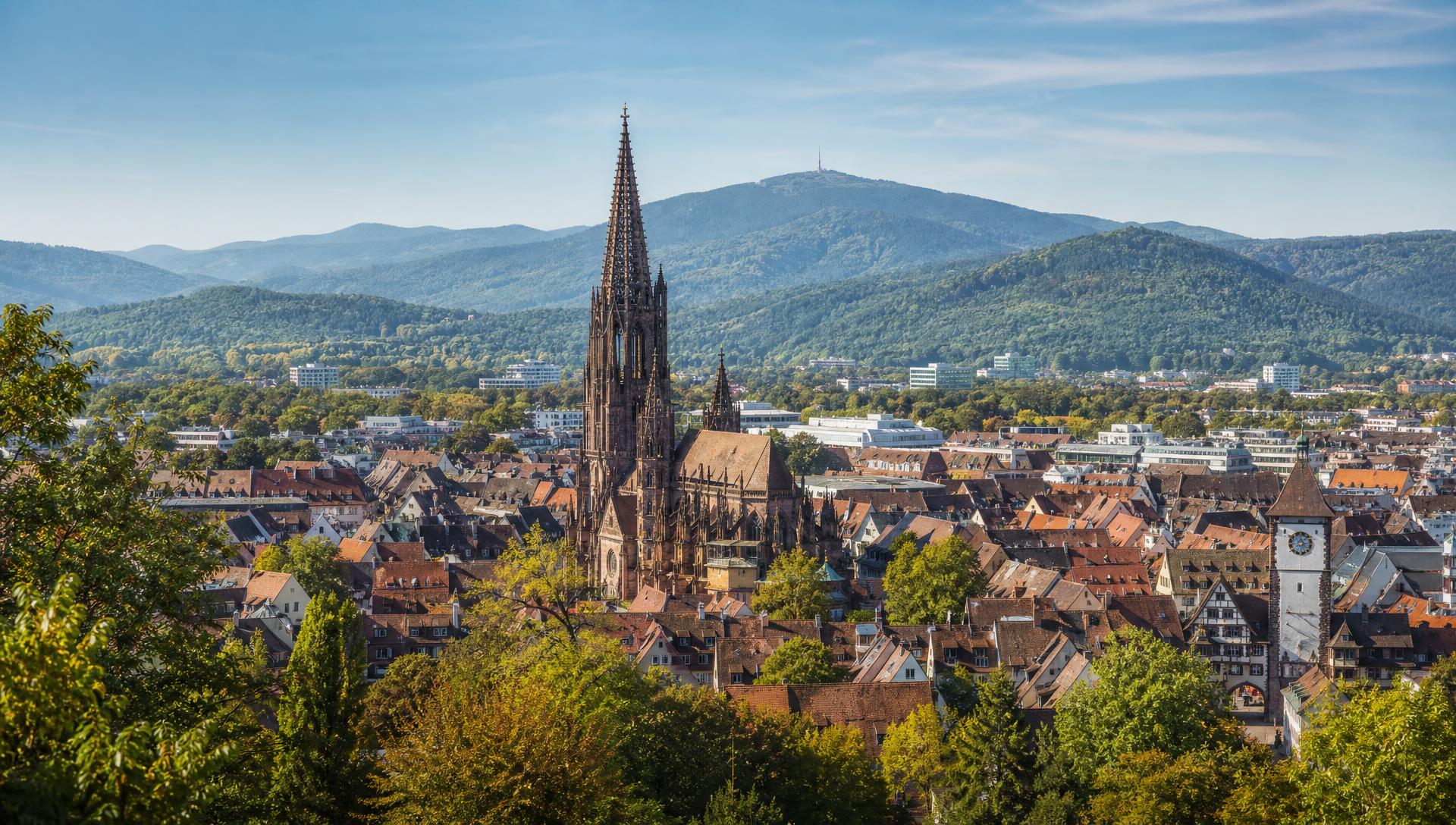 Blick über die Freiburger Altstadt mit dem Turm des Freiburger Münsters und den Hügeln des Schwarzwalds